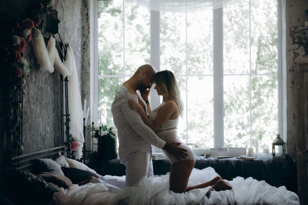 A man and a woman on a bed in front of a sunny window